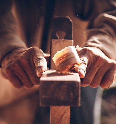 an older carpenter, like Jesus, shaving wood with a plane