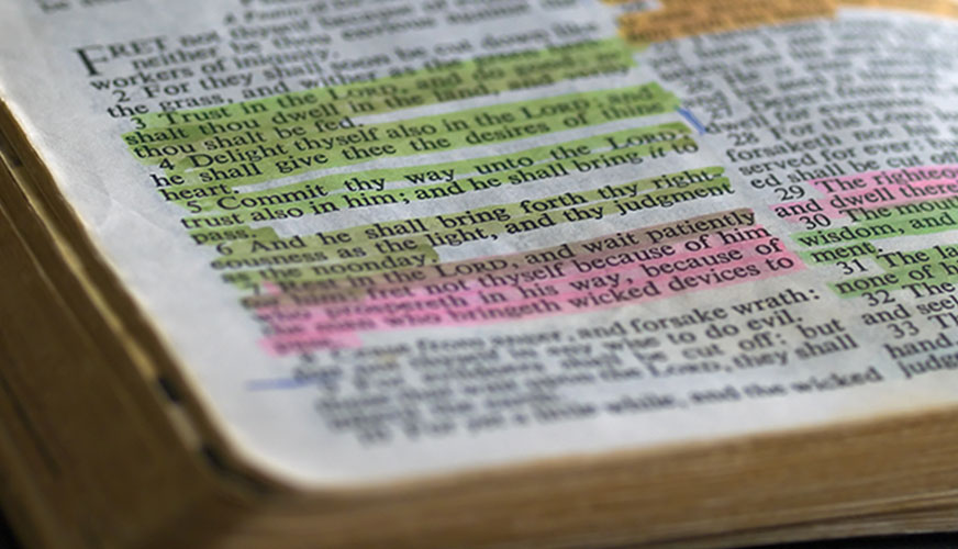 a close up of an old Bible with passages highlightd in green, pink, and orange