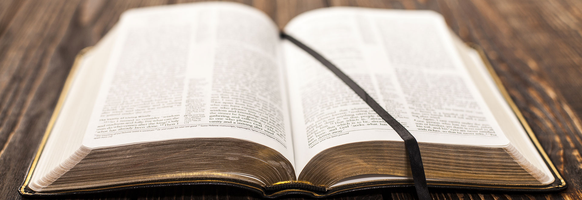 an old Bible with gold dilt pages laying open on a wooden table with a satin ribbon page marker