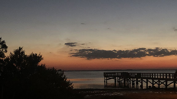 a pier framed on the right at disk with sunset tones over the water