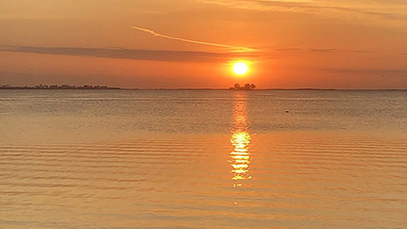 a large calm expanse of ocean with the sun setting overhead
